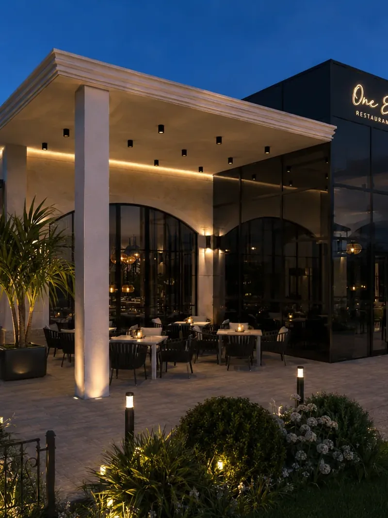 Restaurant terrace at dusk beneath a stone canopy, with arched glazing and outdoor dining tables